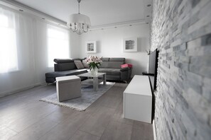 A modern living room with a grey sofa, a coffee table with a vase, a white ottoman, and a brick accent wall.