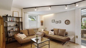 Una sala de estar con dos sofás, una mesita de centro, una estantería y una ventana con cortinas.
