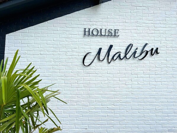 Un mur en briques blanches sur lequel on peut lire, en lettres métalliques, les mots « HOUSE Malibu ».