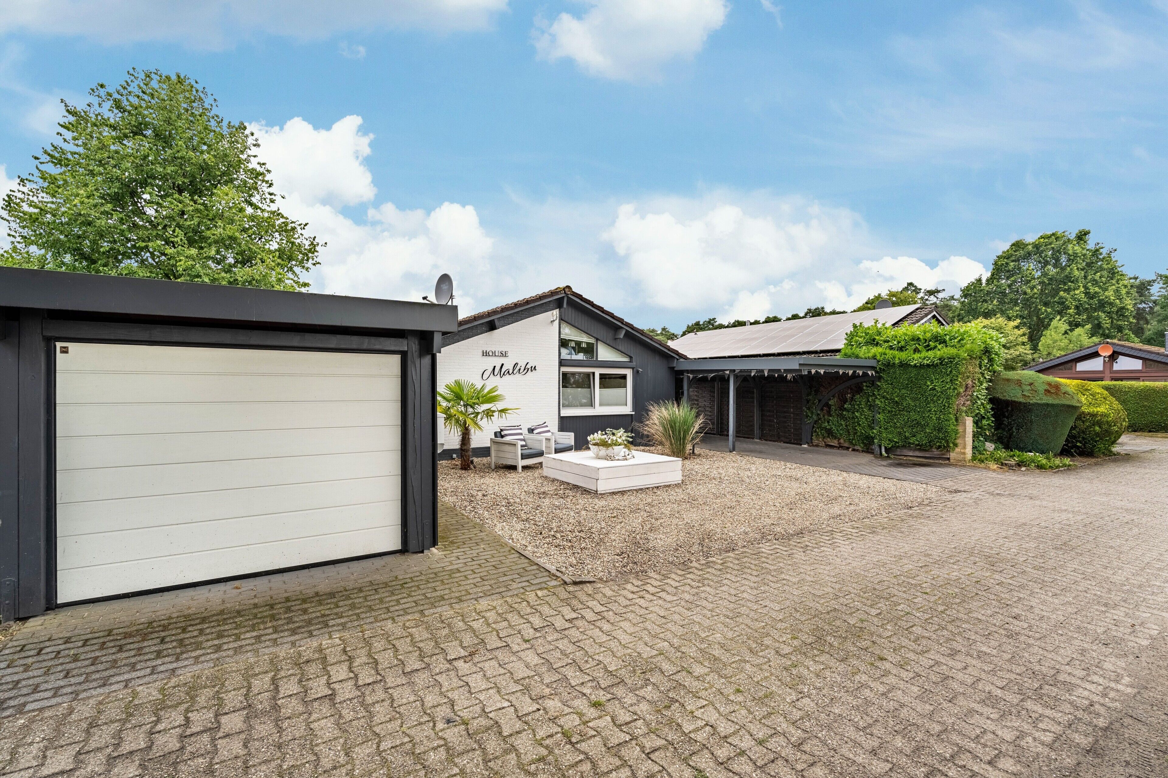 Et hus med garage, terrasse med siddepladser og en have.
