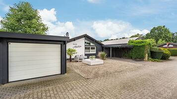 Et hus med garage, terrasse med siddepladser og en have.