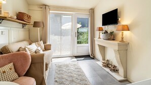 A living room with a sofa, a television, a fireplace, and a view through the glass doors. - Studio Malibu S by the Lake (Wettringen)