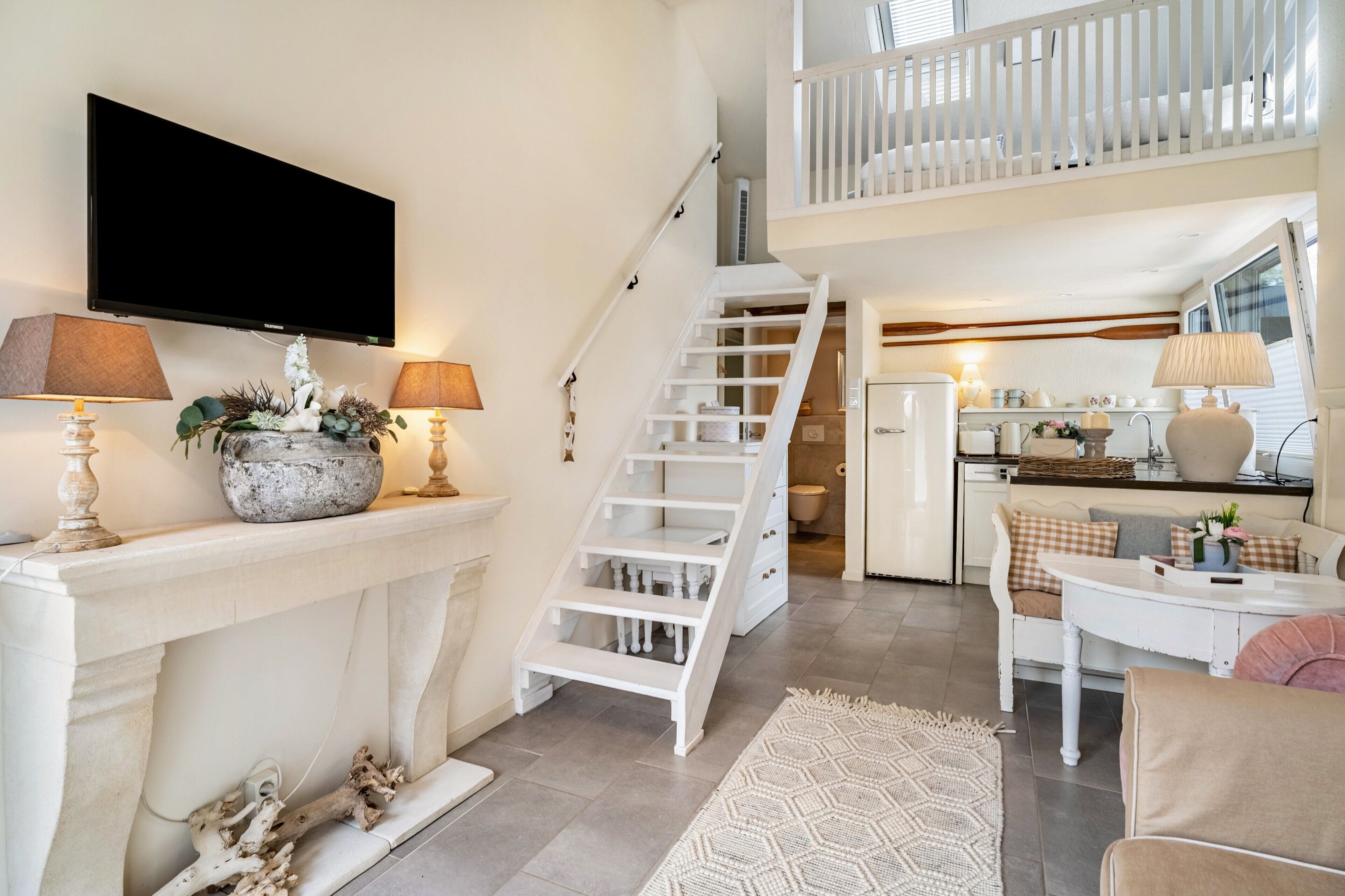 A modern living room with a fireplace, a staircase, a kitchen, and a balcony.