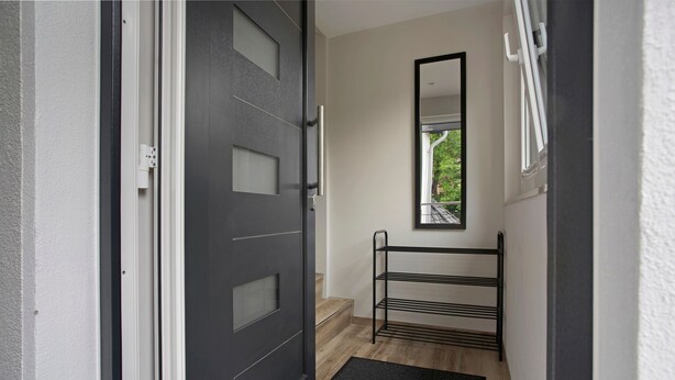 A hallway with a black door, a metal rack, and a window with a view of greenery.