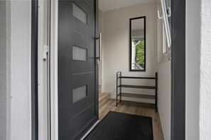 A hallway with a black door, a metal rack, and a window with a view of greenery.