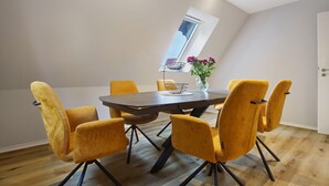 A dining area with a round table, six yellow chairs, a vase with flowers, and a window with a view.
