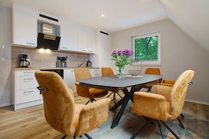 Une cuisine moderne avec des meubles blancs, une table à manger avec des chaises et une fenêtre donnant sur les arbres.