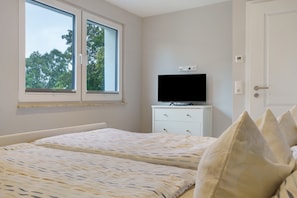 Une chambre avec deux lits, un téléviseur posé sur une commode, une fenêtre et une porte.