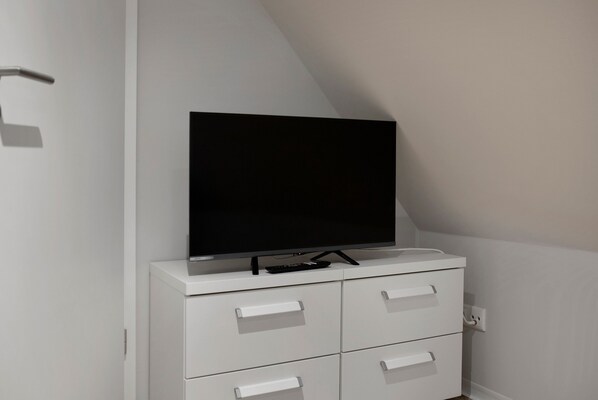 A white TV stand with a flat-screen TV, a remote control, and a power outlet.