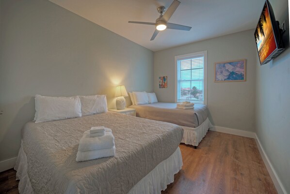A bedroom with two beds, a ceiling fan, a window with blinds, and a painting on the wall.
