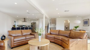 A modern living room with two brown leather sofas, a wooden coffee table, and a kitchen in the background. - Private Pool | 2 Firepits | Peloton | Mtn Views | The Lake House at Malibu (Agoura Hills)