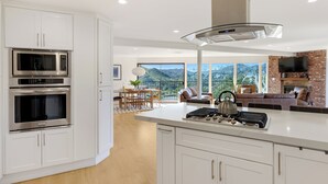 A modern kitchen with built-in appliances, a large island, and a dining area with a view. - Private Pool | 2 Firepits | Peloton | Mtn Views | The Lake House at Malibu (Agoura Hills)