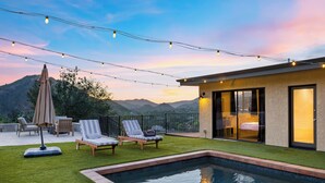 A modern outdoor pool area with a view of mountains, a covered patio with seating, and string lights. - Private Pool | 2 Firepits | Peloton | Mtn Views | The Lake House at Malibu (Agoura Hills)