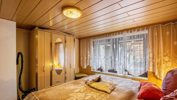 Un dormitorio con cama, armario, ventana con cortinas y una lámpara en el techo.