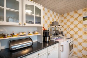Une cuisine avec des meubles blancs, un grille-pain, une machine à café et un réfrigérateur.
