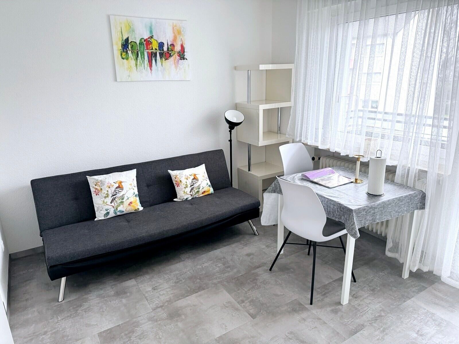 A modern living space with a grey sofa, white chairs, a small table, and a painting on the wall.