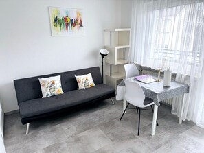 A modern living space with a grey sofa, white chairs, a small table, and a painting on the wall. - Apartment 'Belchen' with Balcony and Wi-Fi (Bad Krozingen)