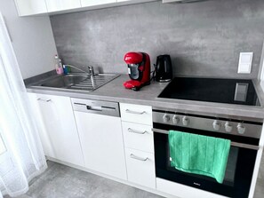 A kitchen with a dishwasher, a red coffee maker, a black coffee pot, and a stove with a green towel hanging on the oven door. - Apartment 'Belchen' with Balcony and Wi-Fi (Bad Krozingen)
