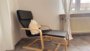 A black chair with wooden legs and a cushion, positioned near a window with a radiator and curtains. - Apartment 'Belchen' with Balcony and Wi-Fi (Bad Krozingen)