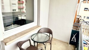 A balcony with a glass table and wicker chairs, a window overlooking a building, and a metal railing. - Apartment 'Belchen' with Balcony and Wi-Fi (Bad Krozingen)