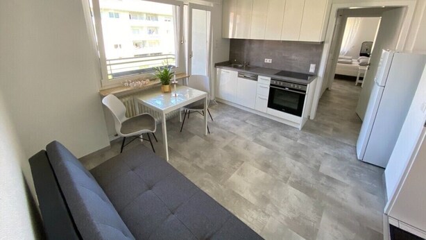 A compact kitchen with white cabinets, a dining area with a table and chairs, and a sofa. - Apartment 'Belchen' with Balcony and Wi-Fi (Bad Krozingen)