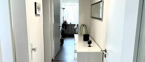 A hallway with a wooden floor, white walls, a ceiling light, and a door on the right.