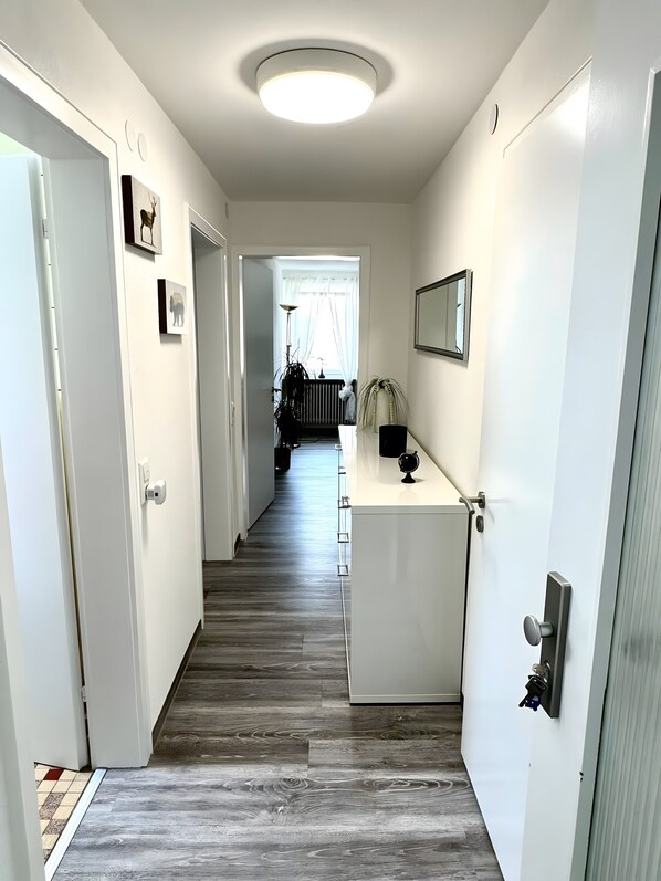 A hallway with a wooden floor, white walls, a ceiling light, and a door on the right.