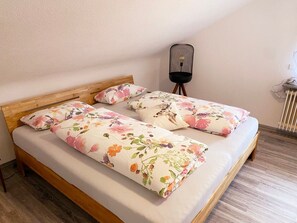Un lit double avec une literie à motifs floraux, une tête de lit en bois et une lampe de chevet.