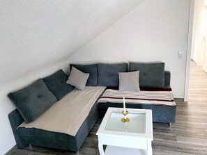 Un canapé d’angle avec une table basse en verre et un plaid à rayures.