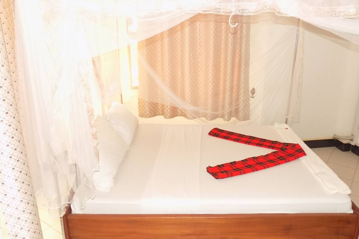 A single bed with a white mattress and a wooden headboard, covered by a white canopy with lace trim.