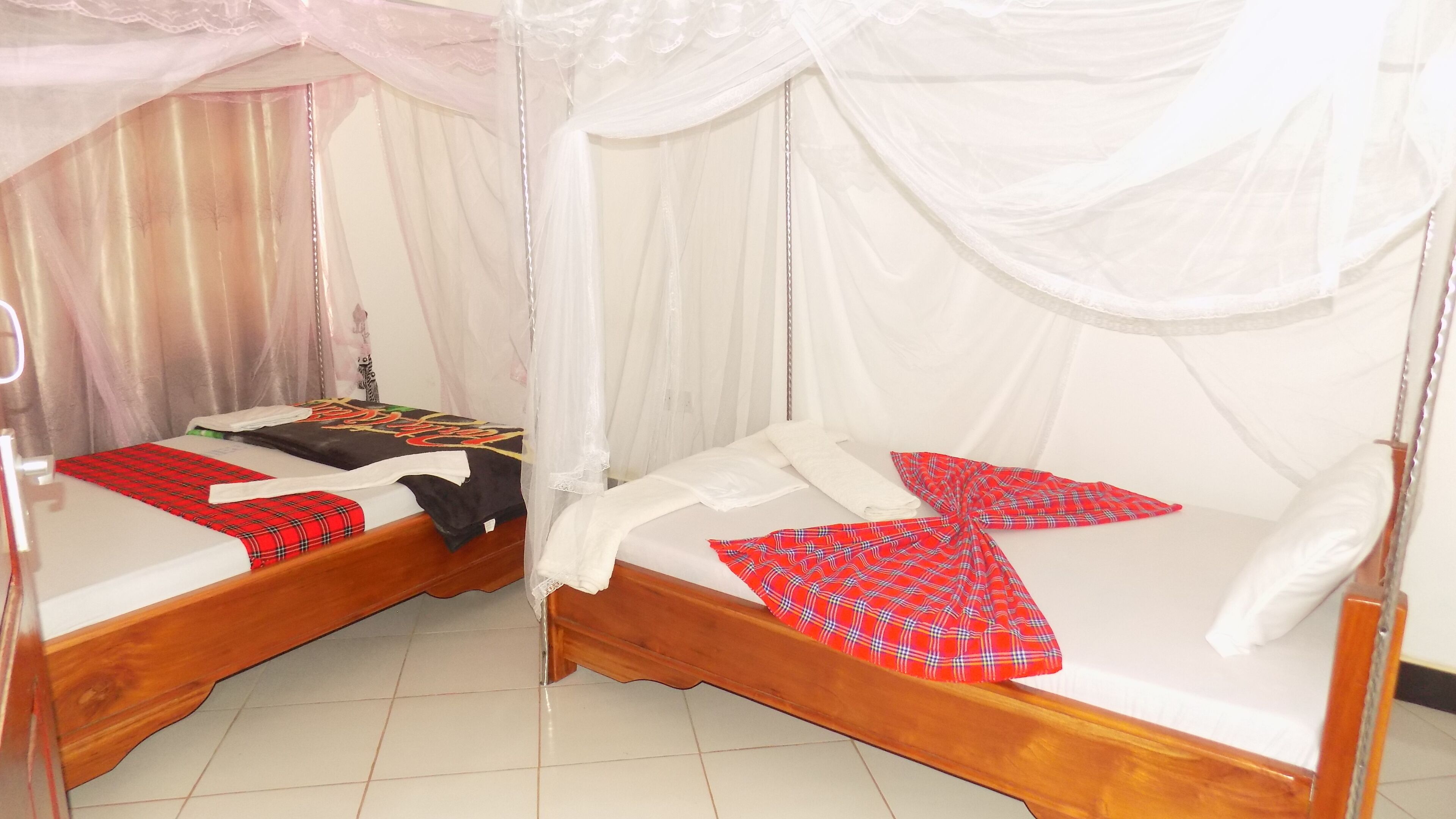 Een kamer met twee houten bedden, elk voorzien van een hemelbedovertrek en een rood geruit plaid.