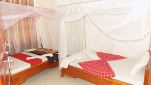 Deux lits en bois, recouverts de draps blancs et de couvertures à carreaux rouges, sont séparés par un ciel de lit blanc.