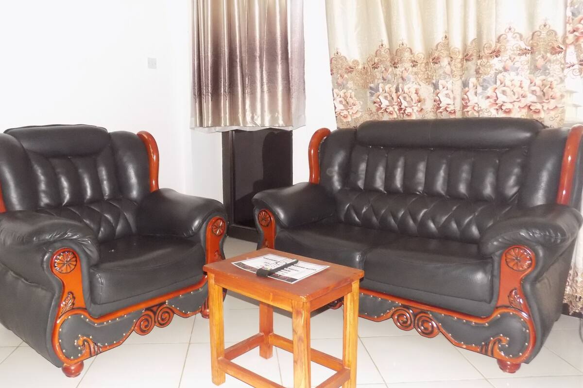 Two black leather armchairs with wooden legs and ornate trim, a small wooden table, and a curtain with a floral pattern.
