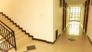 A staircase with black railings leading to a landing. The floor has a checkered pattern of light and dark tiles.