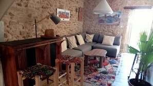Un salón acogedor con pared de piedra, un sofá, una mesa de centro, una pequeña mesa de madera, un tapete colorido y una planta en maceta.