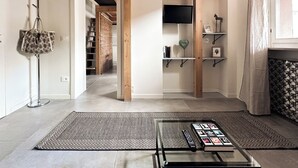 A modern living room with a glass coffee table, wooden beams, a TV, and shelves with decorative items.