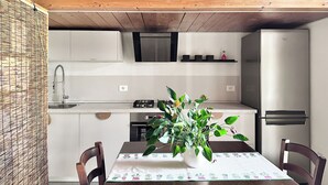 A modern kitchen with wooden ceiling beams, a stainless steel refrigerator, and a dining table with a plant centerpiece.