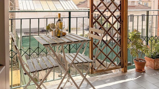 A balcony with a table and chairs, a potted plant, and a view of buildings.