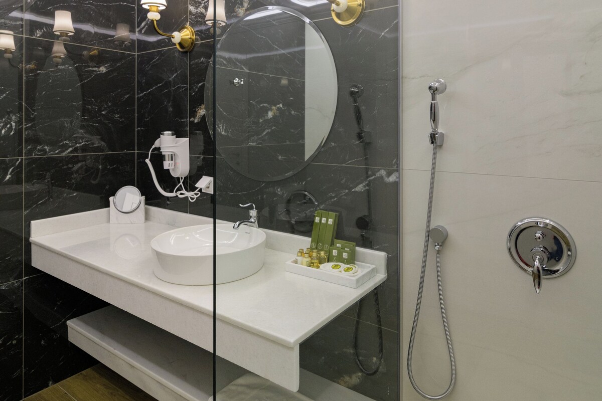 A modern bathroom with a glass-enclosed vanity, a round mirror, a showerhead, and a white sink.