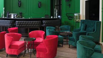 A bar area with green walls, red and teal chairs, and a black leather bar counter.