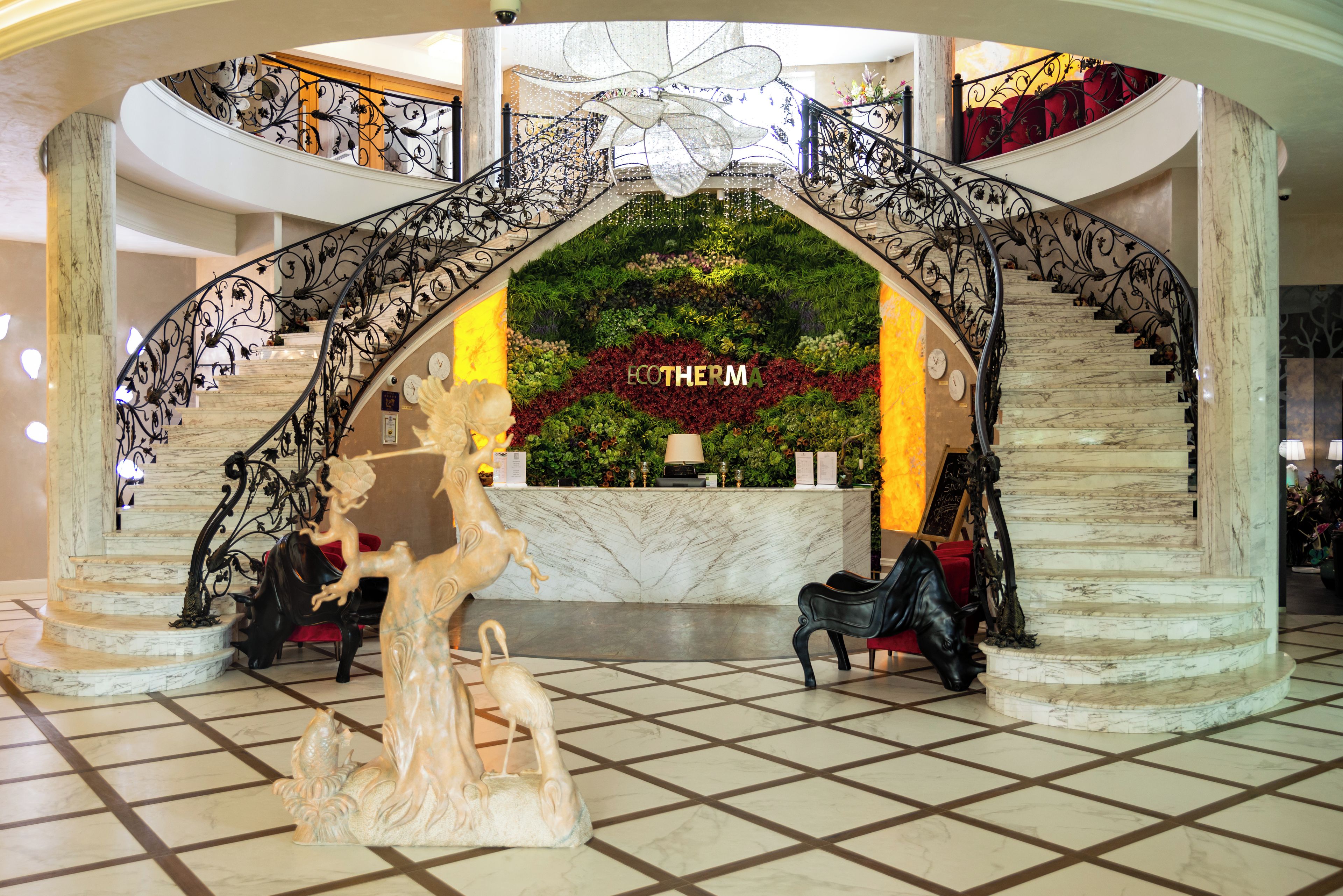 A grand lobby with a marble staircase, a reception desk, and a decorative archway.
