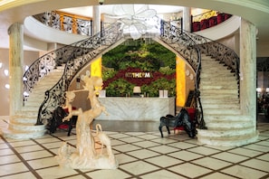 Un lobby espacioso con una escalinata de mármol, una recepción y un arco decorativo.