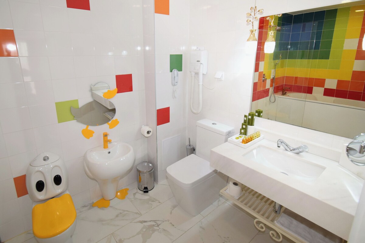 A bathroom with a toilet, bidet, sink, and a mirror with a colorful tile backsplash.