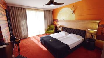 Une chambre d’hôtel avec un grand lit, un fauteuil vert, un bureau et une table de chevet avec une lampe.