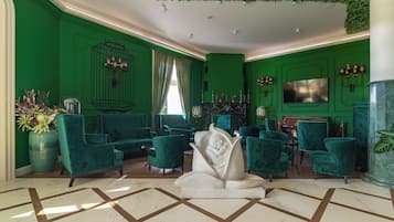 Un hall d’entrée décoré dans des tons de vert, avec des fauteuils confortables, un mur décoré de cages à oiseaux et un sol en marbre.