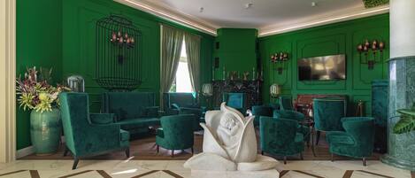Un hall d’entrée décoré dans des tons de vert, avec des fauteuils confortables, un mur décoré de cages à oiseaux et un sol en marbre.