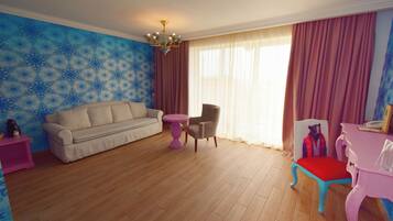 A living room with a beige sofa, a pink table, a chair, and a small table with a teddy bear.