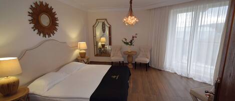 A hotel room with a large bed, a chandelier, a mirror, a small round table, and a chair.