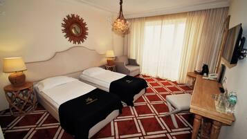 Habitación de hotel con dos camas, un escritorio, una silla, un televisor y un ventanal con cortinas.