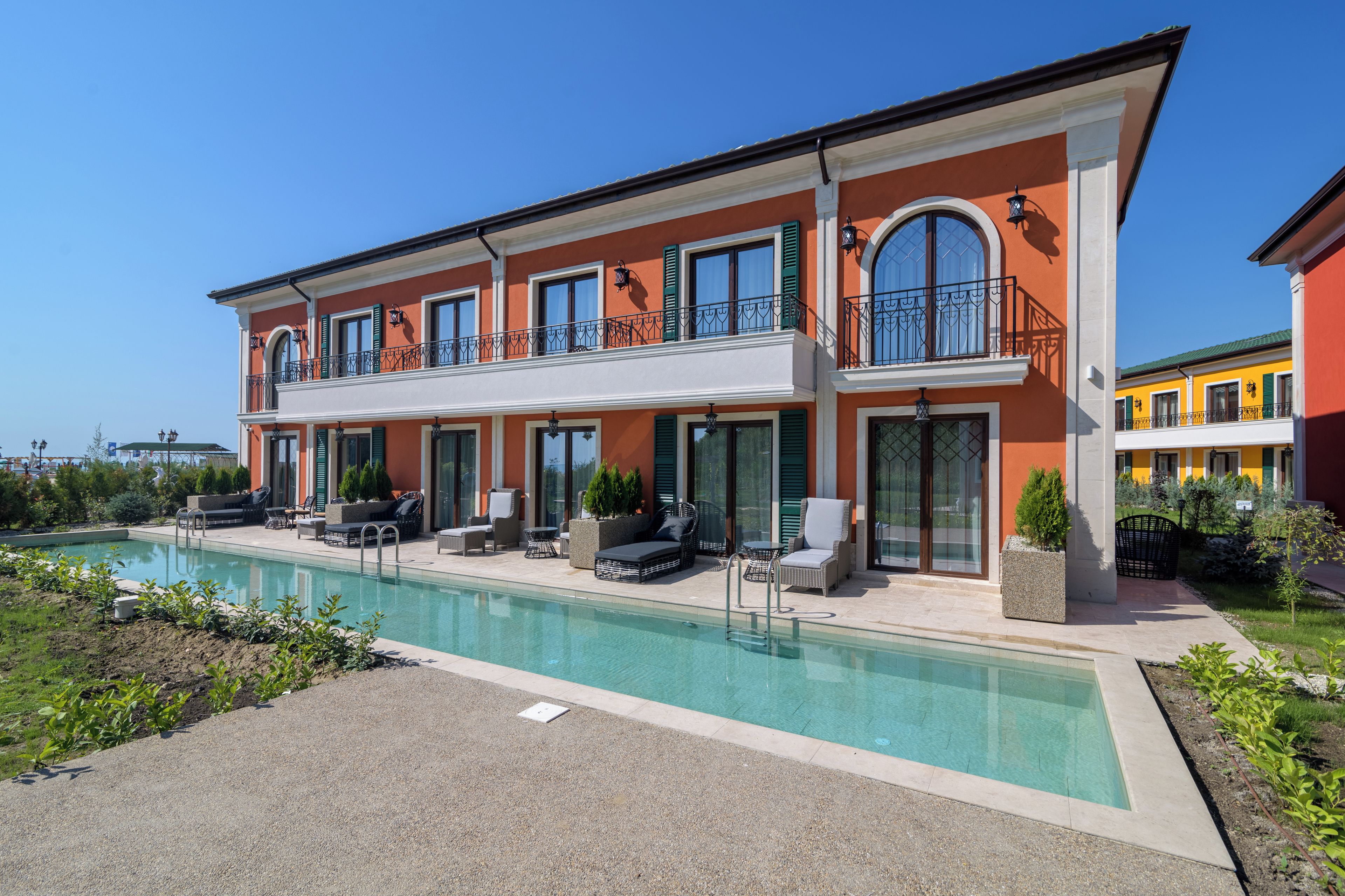 A two-story building with a swimming pool, outdoor seating, and a garden.